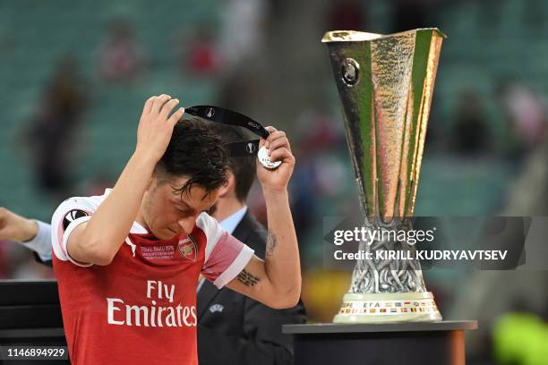 Arsenal's German midfielder Mesut Ozil puts on his medal as he walks past the trophy after losing the UEFA Europa League final football match between...