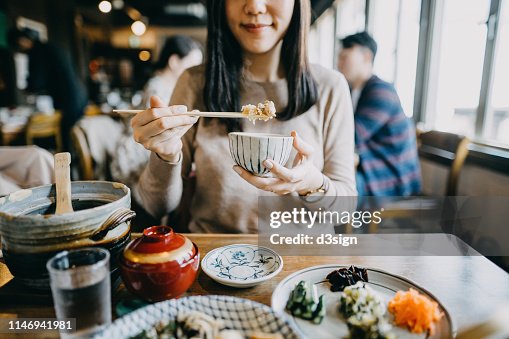 Close up shot of smiling young woman enjoying Japanese cuisine with various side dishes, miso soup and green tea in restaurant Close up shot of smiling young woman enjoying Japanese cuisine with various side dishes, miso soup and green tea in restaurant
