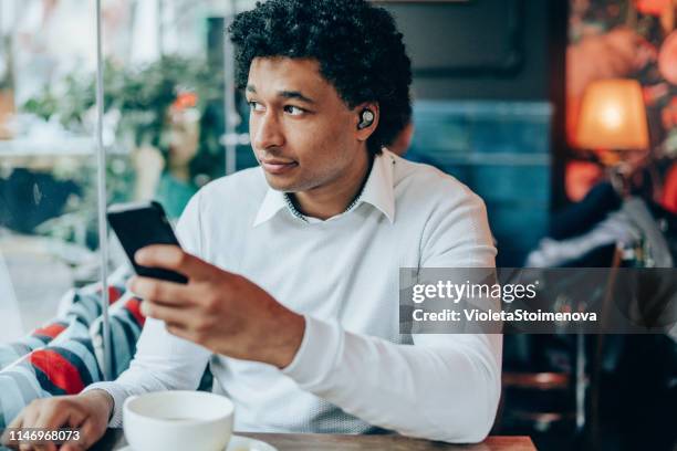 portrait of modern man with wireless earbuds in a cafe - in ear headphones stock pictures, royalty-free photos & images