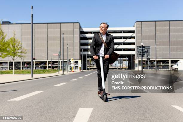 careless businessman is riding on push scooter between office buildings - cooler opa stock-fotos und bilder