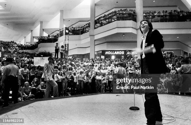 View of American Rock musician Rick Springfield as he stands onstage during a promotional appearance at the Woodfield Mall, Schaumberg, Illinois,...