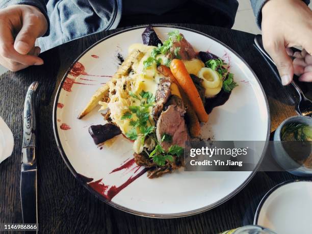 young man enjoying freshly served traditional icelandic food with fork and knife in a restaurant - lamm fleisch stock-fotos und bilder