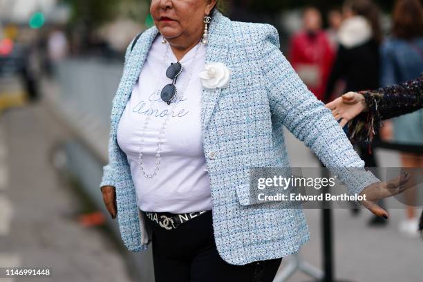 Guest wears Chanel earrings, sunglasses, a white top with the blue inscription "Ciao Amore", a light blue Chanel tweed jacket , a white camellia...