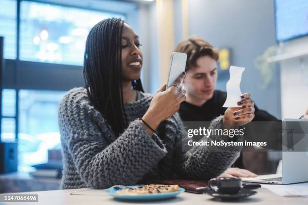 jonge vrouw die een ontvangstbewijs in het café fotografeert - bonnetje stockfoto's en -beelden