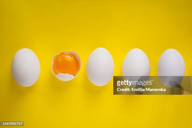 four whole eggs and one broken egg on yellow background - dotter stock-fotos und bilder