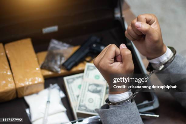 the drug dealer was arrested in handcuffs, drugs money and gun on wooden table in concept about danger and threat of the drug - marijuana arrest stock pictures, royalty-free photos & images