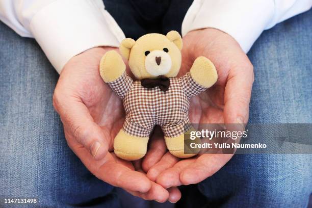 male hands holding a cute teddy bear. man hands in white mittens showing a teddy bear gift dresses in knitted hat and scarf. - woman hands in mittens stock-fotos und bilder