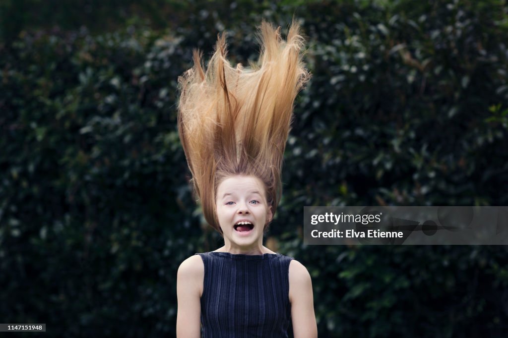 Offbeat portrait of girl (12-13) in a back yard with tangled long fair hair blowing up above her