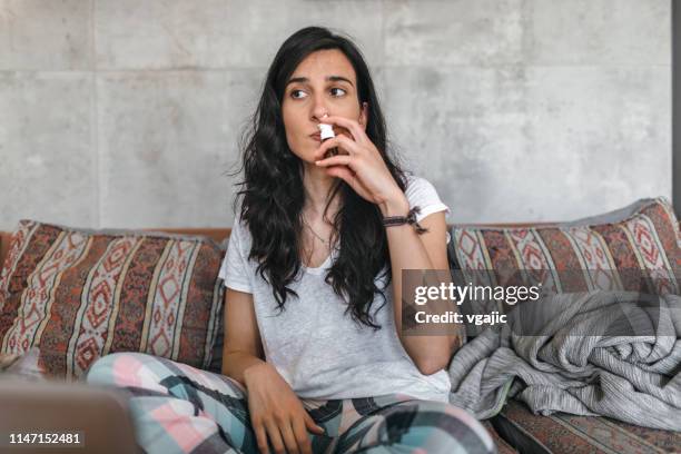 junge frau krank zu hause - nasenspray stock-fotos und bilder