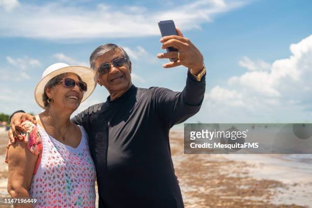 senior couple taking a selfie on the beach - couple on beach sunglasses stock pictures, royalty-free photos & images