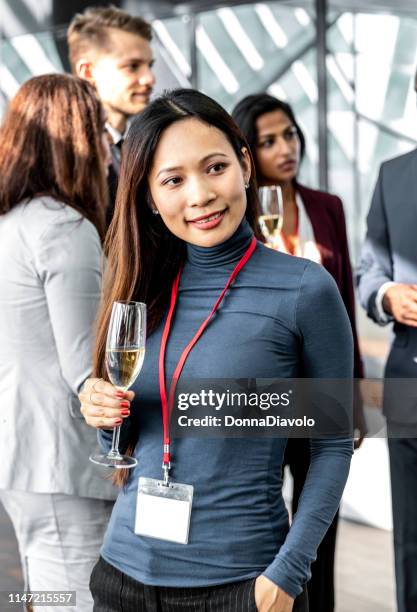 attraktive asiatische frau mit einem glas champange mit mitarbeitern im hintergrund - donna elegante stock-fotos und bilder