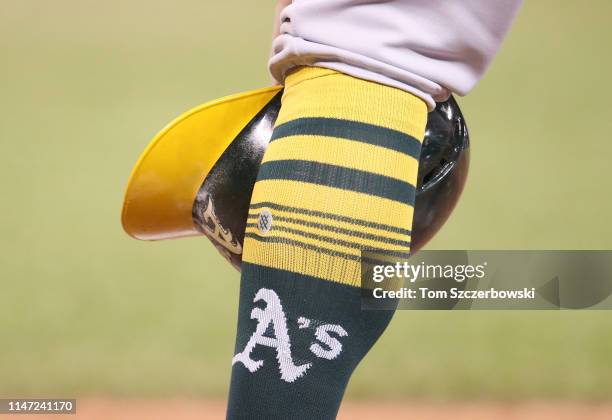 Robbie Grossman of the Oakland Athletics waits during a pitching change as he rests his helmet beside his sock showing the team logo in the eleventh...