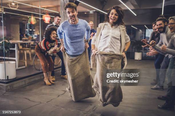 playful entrepreneurs having fun during a sack race at casual office. - sack race stock pictures, royalty-free photos & images