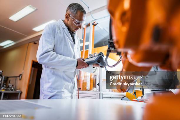 mid adult male engineer working on robotic arm in a research laboratory. - intelligent automation stock pictures, royalty-free photos & images