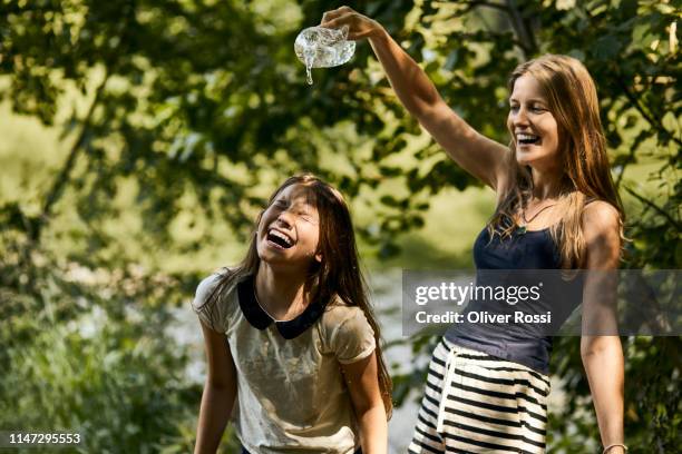 carefree mother and daughter splashing with water bottle in summer - women in wet tee shirts stock pictures, royalty-free photos & images