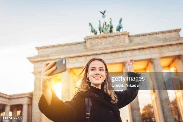 jonge vrouw die selfie bij brandenburger gate in berlijn - internationaal monument stockfoto's en -beelden