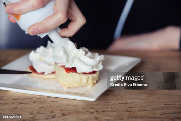 teenager squirting whipped cream from a can onto freshly baked scones - squirting stock pictures, royalty-free photos & images