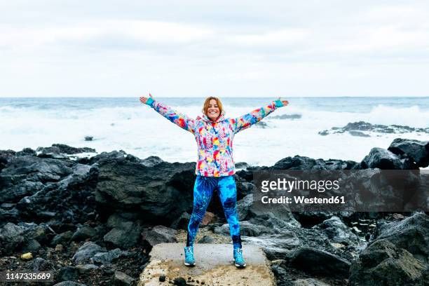 portugal, azores islands, sao miguel, woman with arms raised with the sea in the background in rocky landscape - azores people stock pictures, royalty-free photos & images