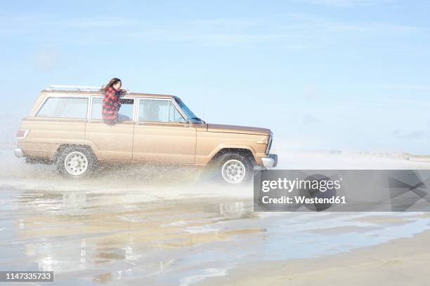 germany, st peter-ording, girl leaning out of window of off-road vehicle driving through water on the beach - car splashing stock pictures, royalty-free photos & images