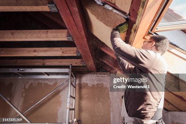 roof insulation, worker filling pitched roof with wood fibre insulation - house insulation not posing stock pictures, royalty-free photos & images