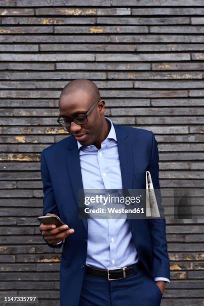 portrait of smiling businessman with newspaper wearing glasses and blue suit looking at mobile phone - business people and paper imagens e fotografias de stock