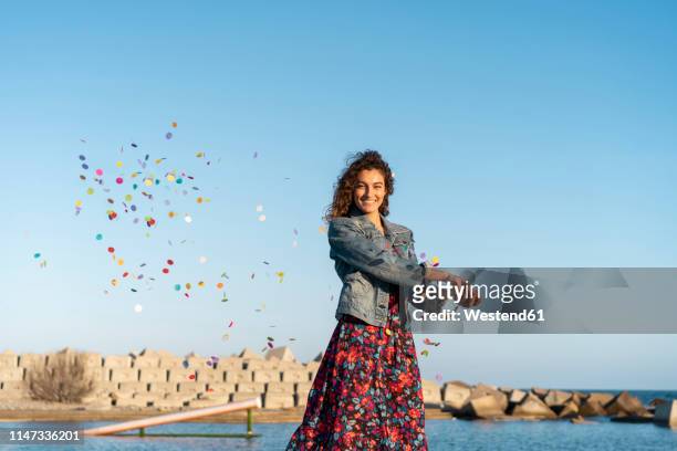 portrait of smiling young woman throwing confetti in the air - floral pattern jacket stock-fotos und bilder