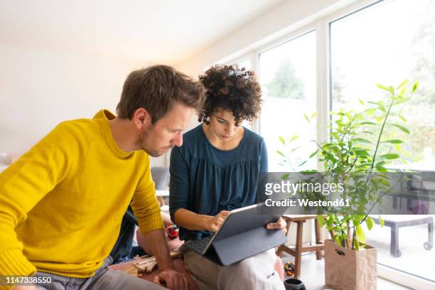 couple sitting in living room, using digital tablet - searching the web imagens e fotografias de stock