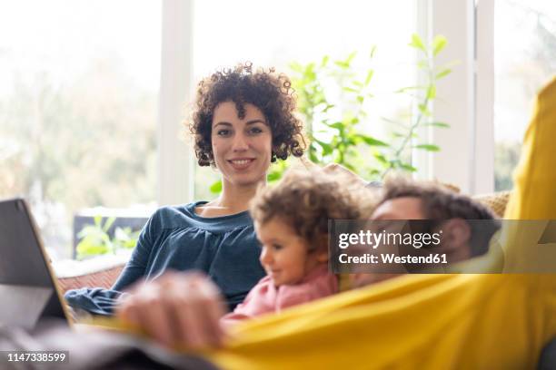 family lying on couch watching movie on theit tablet - family looking at camera stock pictures, royalty-free photos & images