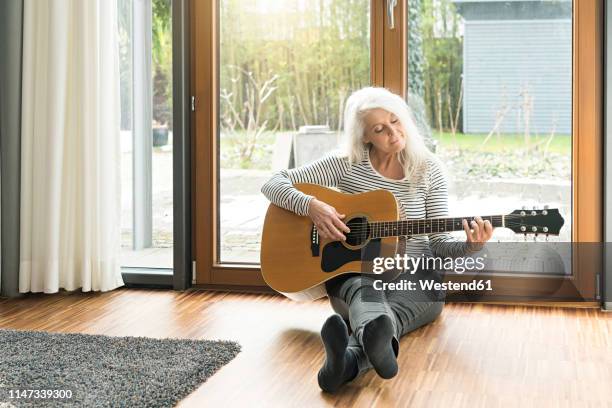 mature woman sitting on the floor of living room playing guitar - woman playing guitar stock pictures, royalty-free photos & images