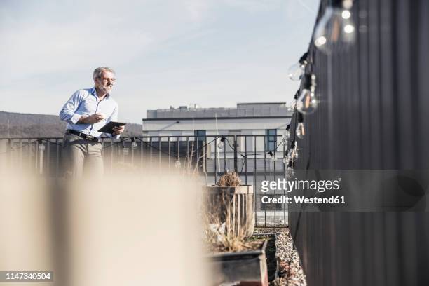 mature businessman with tablet standing on roof terrace - dachterasse stock-fotos und bilder