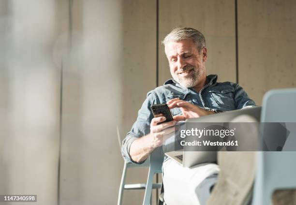 smiling casual mature businessman with laptop and cell phone - business man looking at laptop stock-fotos und bilder