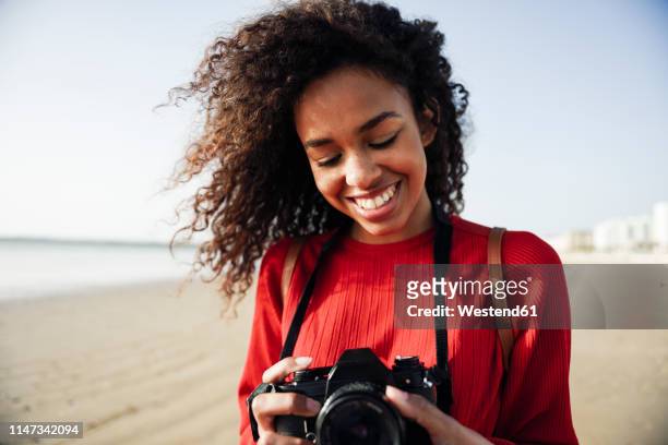 smiling young woman looking at camera on the beach - digitale spiegelreflexcamera stockfoto's en -beelden