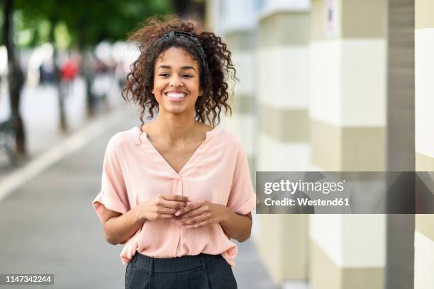 portrait of smiling young woman in the city - rosa bluse stock-fotos und bilder