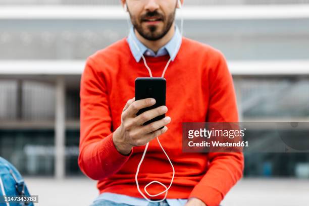 casual businessman sitting on a bench in the city, using his smartohone and earphones - red headphones stock pictures, royalty-free photos & images