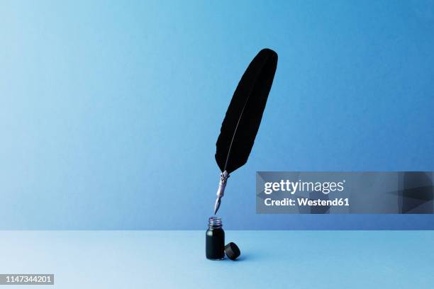 quill pen and inkwell over blue background - pluma de ave fotografías e imágenes de stock