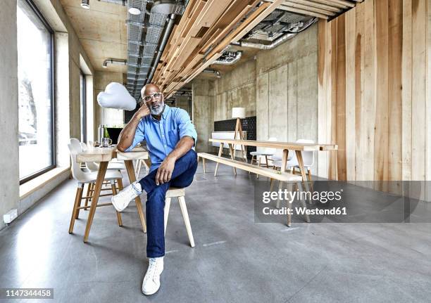 mature businessman sitting in modern office with cloud balloon - büro und wolke stock-fotos und bilder