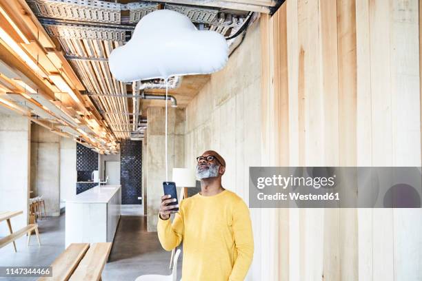 mature businessman holding cell phone attached to cloud balloon - hovering fotografías e imágenes de stock