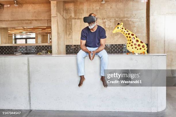 mature businessman in modern office sitting next to giraffe figurine wearing vr glasses - barefoot black men stock pictures, royalty-free photos & images