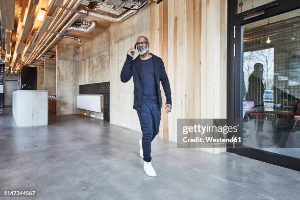 mature businessman on cell phone walking in modern office - veste homme photos et images de collection