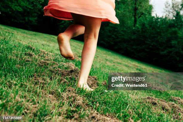 back view of girl running barefoot on a meadow, partial view - girl barefoot fotografías e imágenes de stock