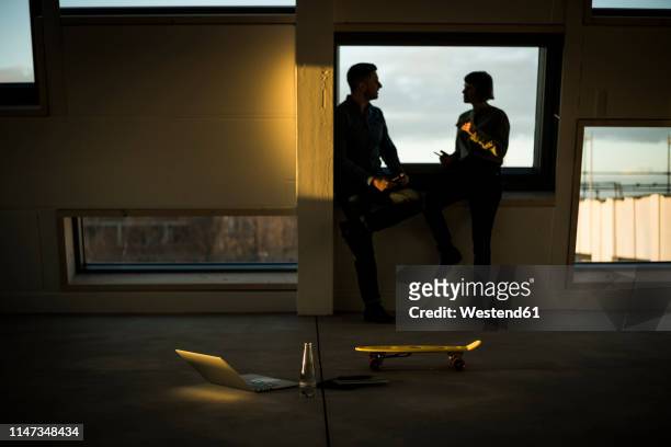 colleagues sitting on window sill, discussing after work - engaged sunset stockfoto's en -beelden