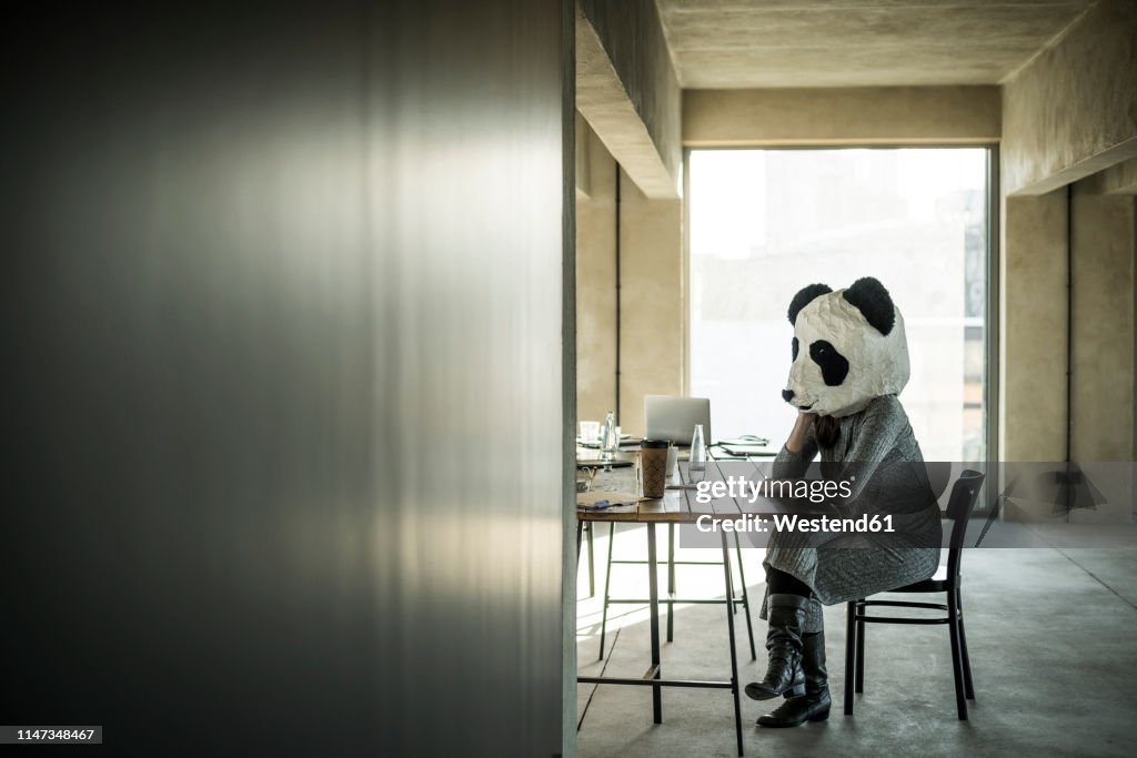 Woman with panda mask sitting in office, thinking