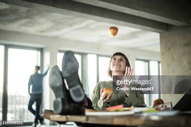 woman juggling apples in the office, sitting with feet on desk - apple company foto e immagini stock