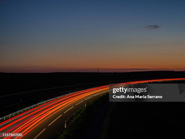 lights and trails of vehicles, cars and trucks, driving along a road with a curve at nightfall. - twilight market stock pictures, royalty-free photos & images