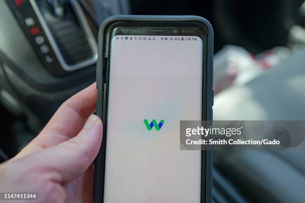 Close-up of hand of a man holding a smartphone with the Waymo app, under testing for future use in calling self driving taxis from driverless...