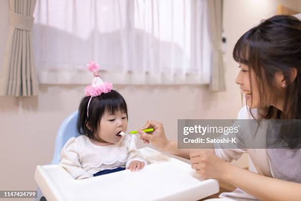 young mother giving yogurt to her baby girl - asian baby eating stock pictures, royalty-free photos & images