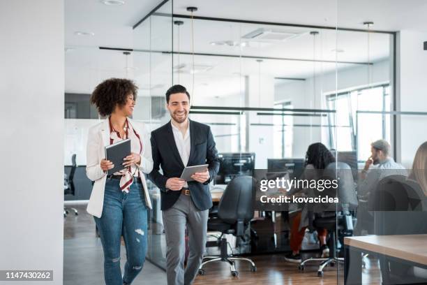 mujer de negocios africana y sus compañeros de trabajo caucásicos utilizando tableta digital y caminar en la oficina - casual chic fotografías e imágenes de stock