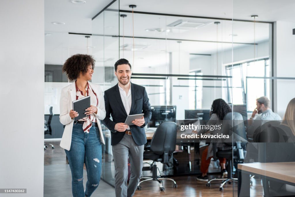 African businesswoman and her Caucasian coworkers using digital tablet and walking in the office