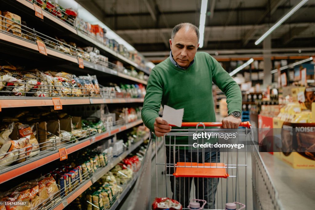 Mann mit Einkaufsliste kauft Lebensmittel im Supermarkt