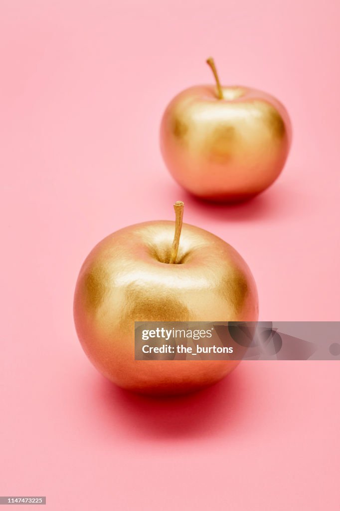 Still life of two golden apples on pink background